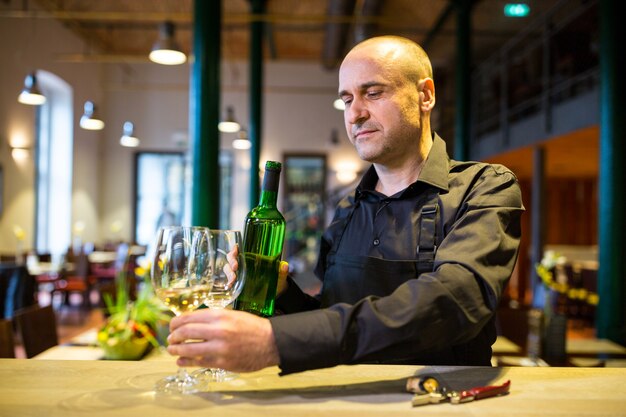 Kelner die glazen en een fles witte wijn houden