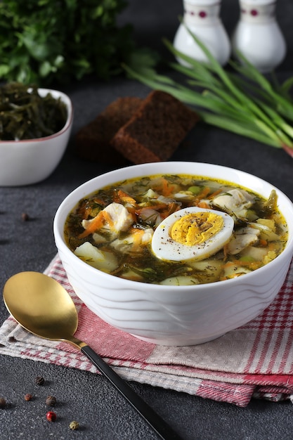 Kelp and chicken soup served with boiled egg in a white bowl on dark gray background. Vertical format