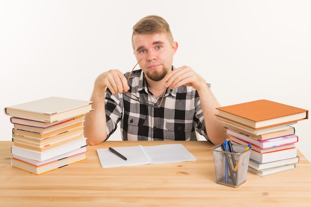 Kennis-, student- en onderwijsconcept - Vermoeide man zit aan de tafel en maakt aantekeningen in een notitieblok