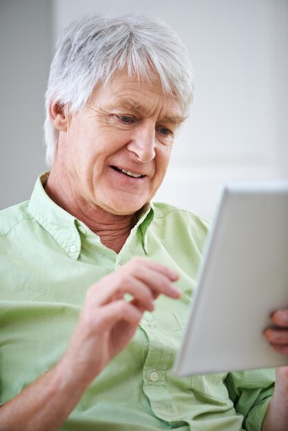 Kennismaken met techniek. Shot van een oudere man die een digitale tablet gebruikt terwijl hij thuis op de bank zit.