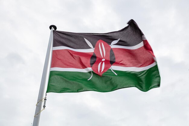 Kenya flag on a pole waving cloudy sky background