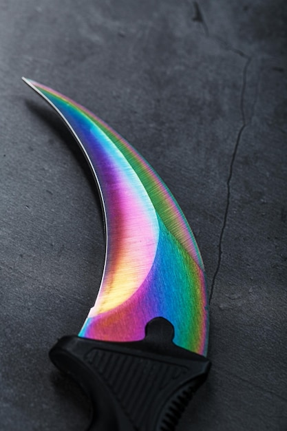 Pugnale kerambit con una lama color arcobaleno su uno sfondo scuro strutturato. armi fredde, spazio libero