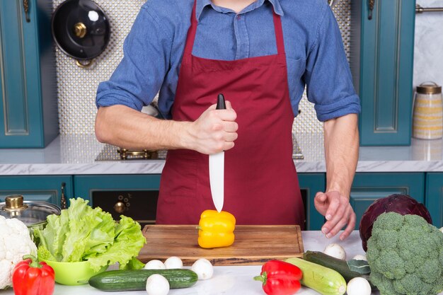 Keramisch mes in de hand gesneden gele paprika groente op een houten bord in de keuken. Vegetarisch, dieet, gezondheidsconcept. Voedselbereiding, koken, culinair, keuken.