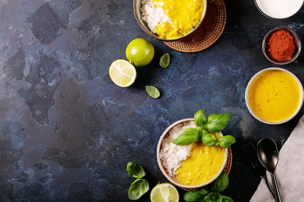 Keramische kom met gele curry geserveerd met basilicum en limoenen