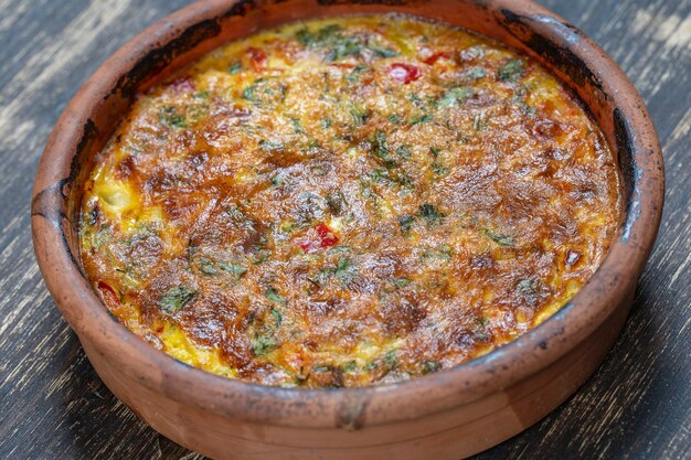 Keramische kom met plantaardige frittata, eenvoudig vegetarisch eten. frittata met tomaat, paprika, ui en kaas op houten tafel, close-up. italiaanse eieromelet, bovenaanzicht