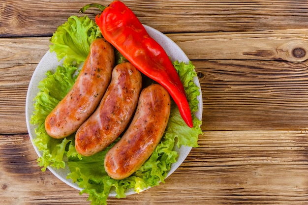 Keramische plaat met gegrilde worstjes, peper en slablaadjes op rustieke houten tafel. Bovenaanzicht