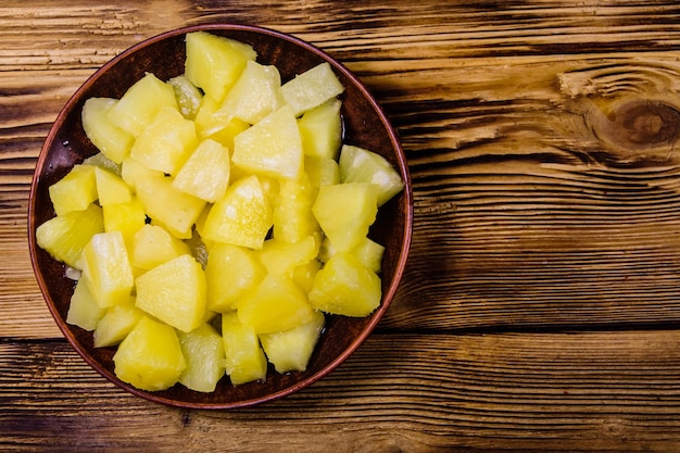 Keramische plaat met gehakte ananas in blik op rustieke houten tafel. Bovenaanzicht