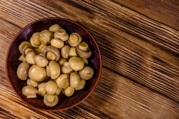 Keramische plaat met ingeblikte champignons op rustieke houten tafel. Bovenaanzicht