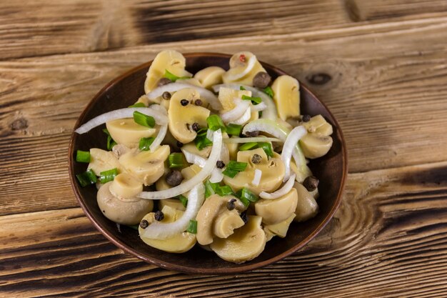 Keramische plaat met ingemaakte champignons. Gemarineerde champignons op houten tafel. Bovenaanzicht