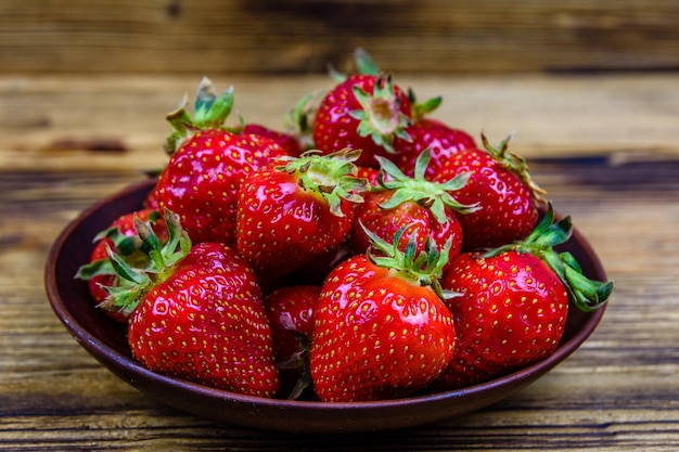 Keramische plaat met stapel rijpe aardbeien op rustieke houten tafel