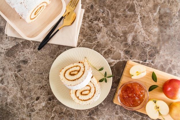 Keramische plaat met twee stukken delicate biscuitrol met appeljam en poedersuiker bakingrediënten bovenaanzicht