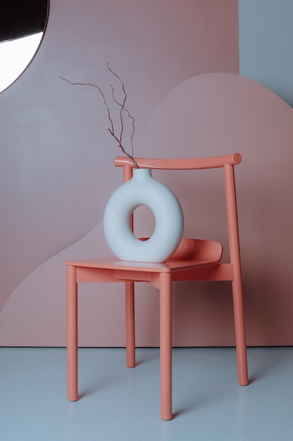 Foto keramische vaas met droge tak staande op een oranje stoel tegen de achtergrond van een creatieve geometrische compositie minimalisme in het interieur