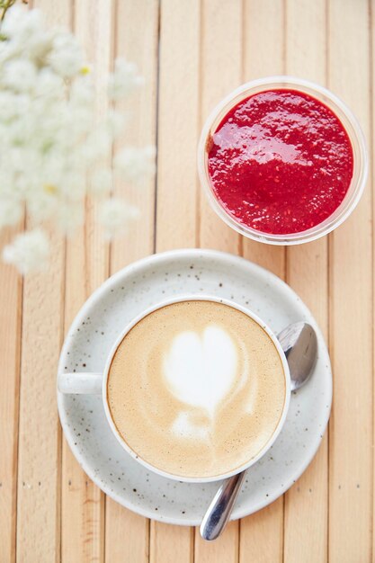 Keramische witte kop cappuccino met hart dessert van frambozenjam voorgerecht licht ontbijt op café terras met wazige voorgrond van kamille bloemen Close up van voedsel verticale foto