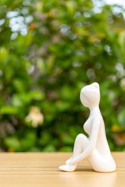 Keramische yoga beeldje van vrouw doet yoga pose op houten vloer en groene blad achtergrond