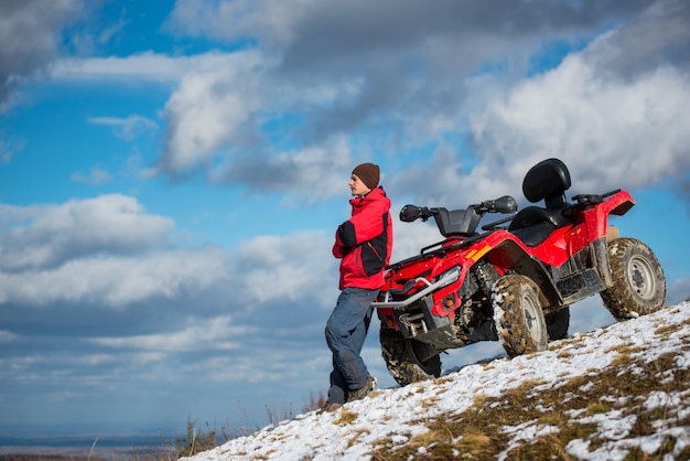 Kerel die zich dichtbij rode ATV-vierlingfiets bevinden op sneeuwberghelling