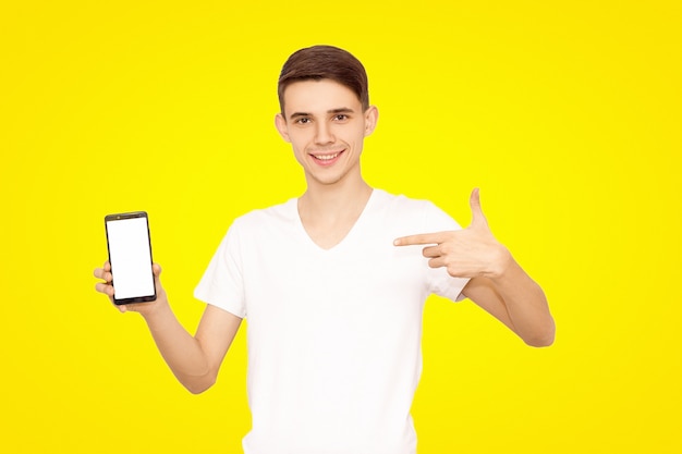 Kerel in een wit T-shirt adverteert de telefoon, geïsoleerd op een gele achtergrond