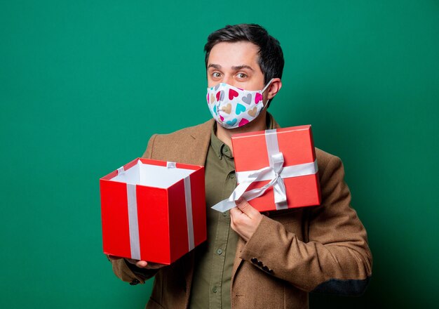 Foto kerel in jasje en gezichtsmasker die giftdoos op groen houden