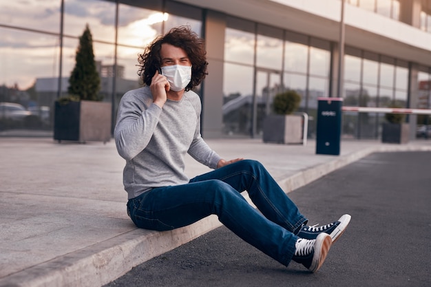 Kerel in masker die op smartphone op straat spreekt