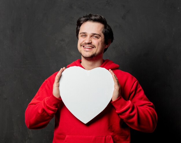 Kerel in rood sweatshirt houdt hartvormframe op donkere muur