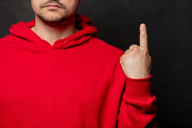 Kerel in rood sweatshirt toont vingerpuntgebaar op donkere muur