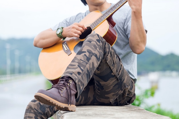 Kerel met gitaar die zich op de dam, ladingsbroek bevindt