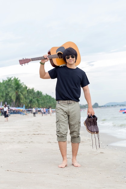 Kerel met gitaar die zich op het strand, ladingsbroek bevindt