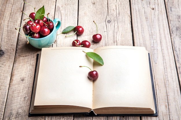 Kers in de prachtige turquoise beker en het oude boek op een houten tafel. fruit, onderwijs