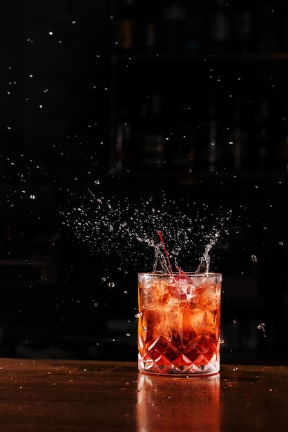 Kersen vallen en spetteren in Negroni alcoholische cocktail Barman bereidt klassieke Negroni cocktail aan de bar