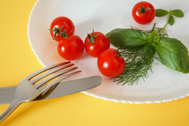 Kersentomaten op een bord met basilicum en bestek