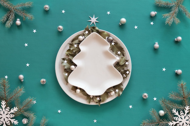 Kerst achtergrond in groen en wit. Kerstboom vorm plaat met kopie-ruimte op tafel bedekt met groene munt textiel. Dennenboomtakjes en witte decoraties. Hulstblaadjes op ronde plaat.