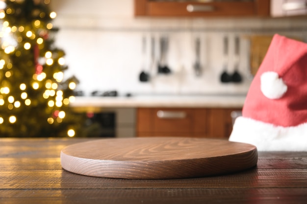 Kerst achtergrond met houten tafelblad, kerstmuts en wazig keuken.