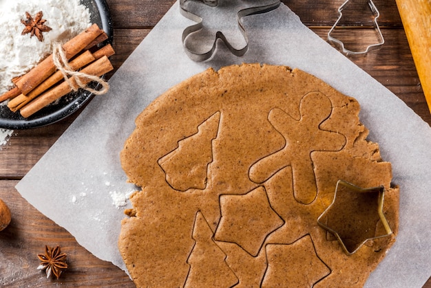 Kerst bakken. Gemberdeeg voor peperkoek, peperkoekmannen, sterren, kerstbomen, deegrol, kruiden (kaneel en anijs), bloem. Op het huis keuken houten tafel. Kopieer ruimte bovenaanzicht