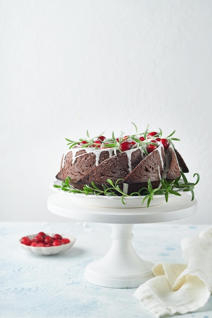 Kerst chocolade bundt cake Traditionele kerstfruitcake met witte glazuur veenbessen en rozemarijn op witte standaard met kerstversiering Winter bakken met Kerstmis of Nieuwjaar Kopieer ruimte