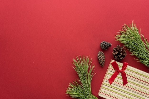 Kerst compositie. Een doos met een geschenk en vuren takken op een rode achtergrond. Vuren kegels en kerstversiering. Platliggend, bovenaanzicht, ruimte voor tekst