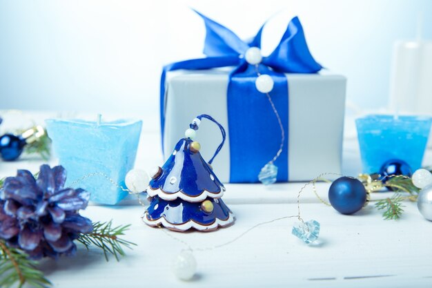 Kerst compositie. verpakt cadeau met blauw lint, dennenappels, vuren takken, handgemaakte kaarsen, xmas blauw decor op een houten witte achtergrond.