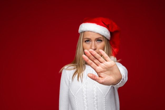 Kerst concept foto van een serieuze dame in kerstmuts haar arm naar voren als een stopbord uitbreiden. vakantie concept