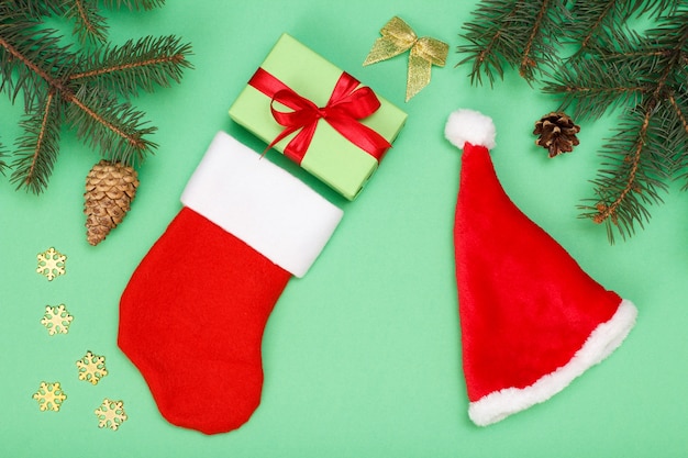 Kerst decoratie. Santa's laars en hoed, geschenkdoos, sparren takken met kegels op groene achtergrond. Bovenaanzicht. Kerst wenskaart concept.