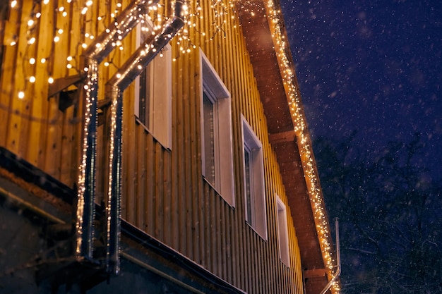 Kerst decoratieve gele slingers lichten vast op het dak van het huis buiten 's avonds kerstversiering