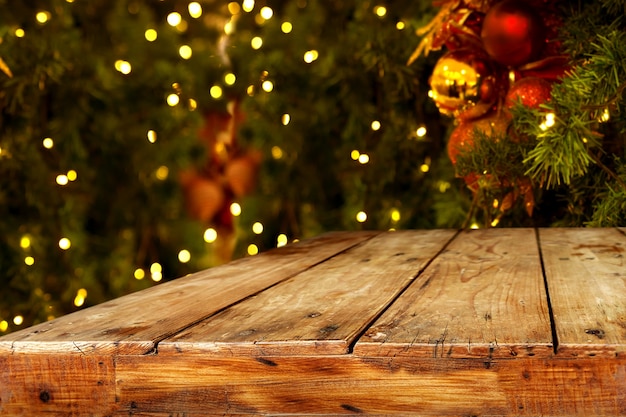 Foto kerst en nieuwjaar achtergrond met lege donkere houten dek tafel over kerstboom en wazig licht bokeh. leeg scherm voor product montage. rustieke vintage kerstmis achtergrond.