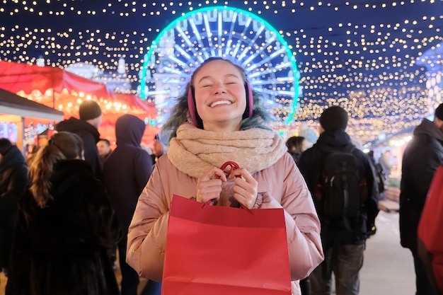 Foto kerst- en nieuwjaarsvakantie, gelukkig tienermeisje met rode boodschappentassen op kerstmarkt