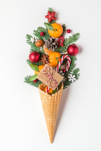 Kerst eten concept. mandarijn fruit, fir tree takken en kerstversiering in wafel-ijsje op witte achtergrond. verticale oriëntatie. bovenaanzicht. plat leggen