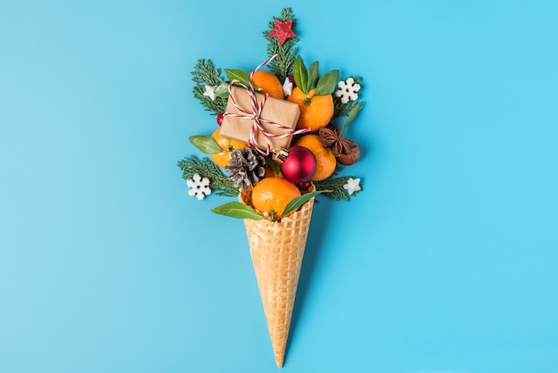 Kerst eten concept. mandarijn fruit, geschenkdoos en kerstversiering in wafel-ijsje op blauwe achtergrond. bovenaanzicht. plat leggen