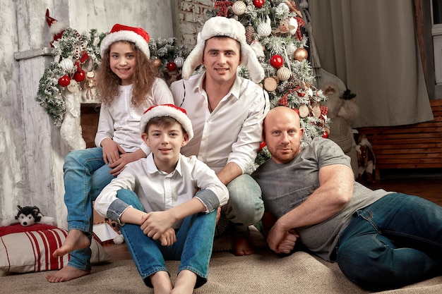 Kerst familie. geluk. portret van vader, moeder en kinderen van verschillende leeftijden zitten op de bank thuis bij de kerstboom en open haard, iedereen lacht.