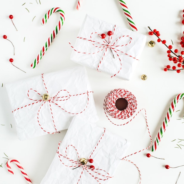 Kerst geschenkdozen met feestelijke snoepjes, tak met rode bessen, haspel van kersttouw en sparrennaalden op witte tafel. plat lag, bovenaanzicht