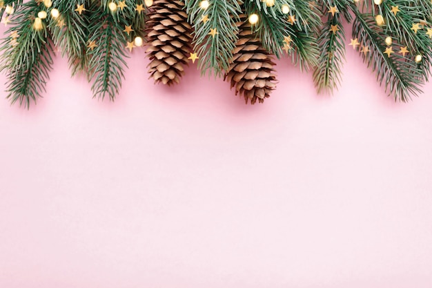 Kerst grens met dennentakken en coniferen kegels op pastel roze achtergrond, kopie ruimte