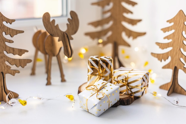 Kerst herten. Decoratieve gouden geschenkdoos en houten rendier speelgoed op witte vensterbank thuis. Gelukkig nieuwjaar 2022. Handgemaakte figuur herten en dennenboom. Eco-stijl doe-het-zelf.