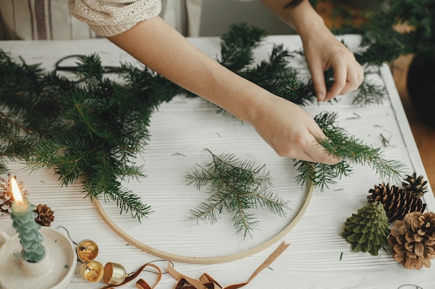 Kerst moderne krans maken vrouwenhanden met dennentakken die krans op ronde hoepel maken