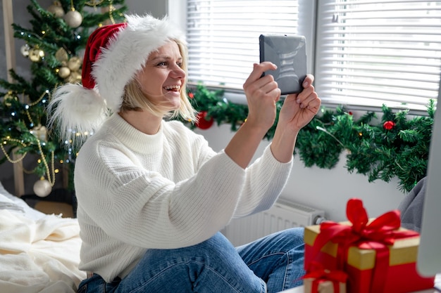 Kerst online gefeliciteerd lachende vrouw met behulp van mobiele tablet voor video-oproep vrienden en ouders