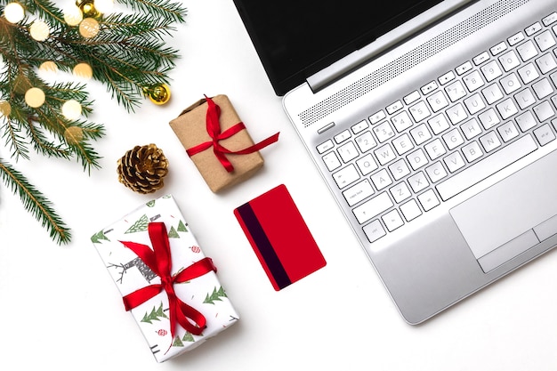 Kerst online winkelen plat leggen. Een geopende laptop, een creditcard, geschenkdozen met een rood lint, groene dennentakken, slingers van sterren