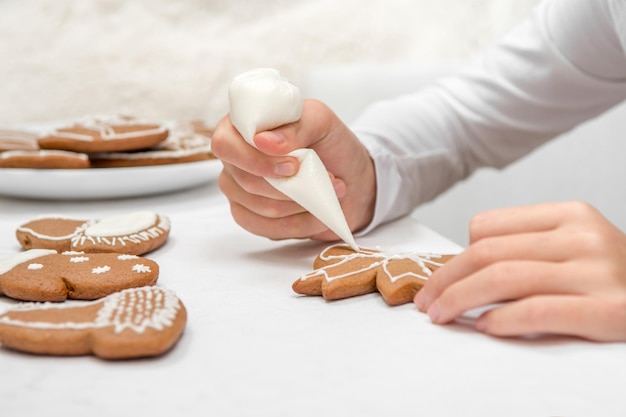 Kerst peperkoek schilderij. het kind gebruikt wit glazuur om een afbeelding op een koekje te schilderen.